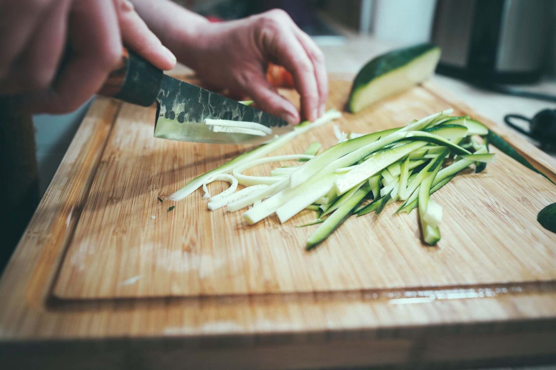 person slicing zucchini on wooden cutting board
