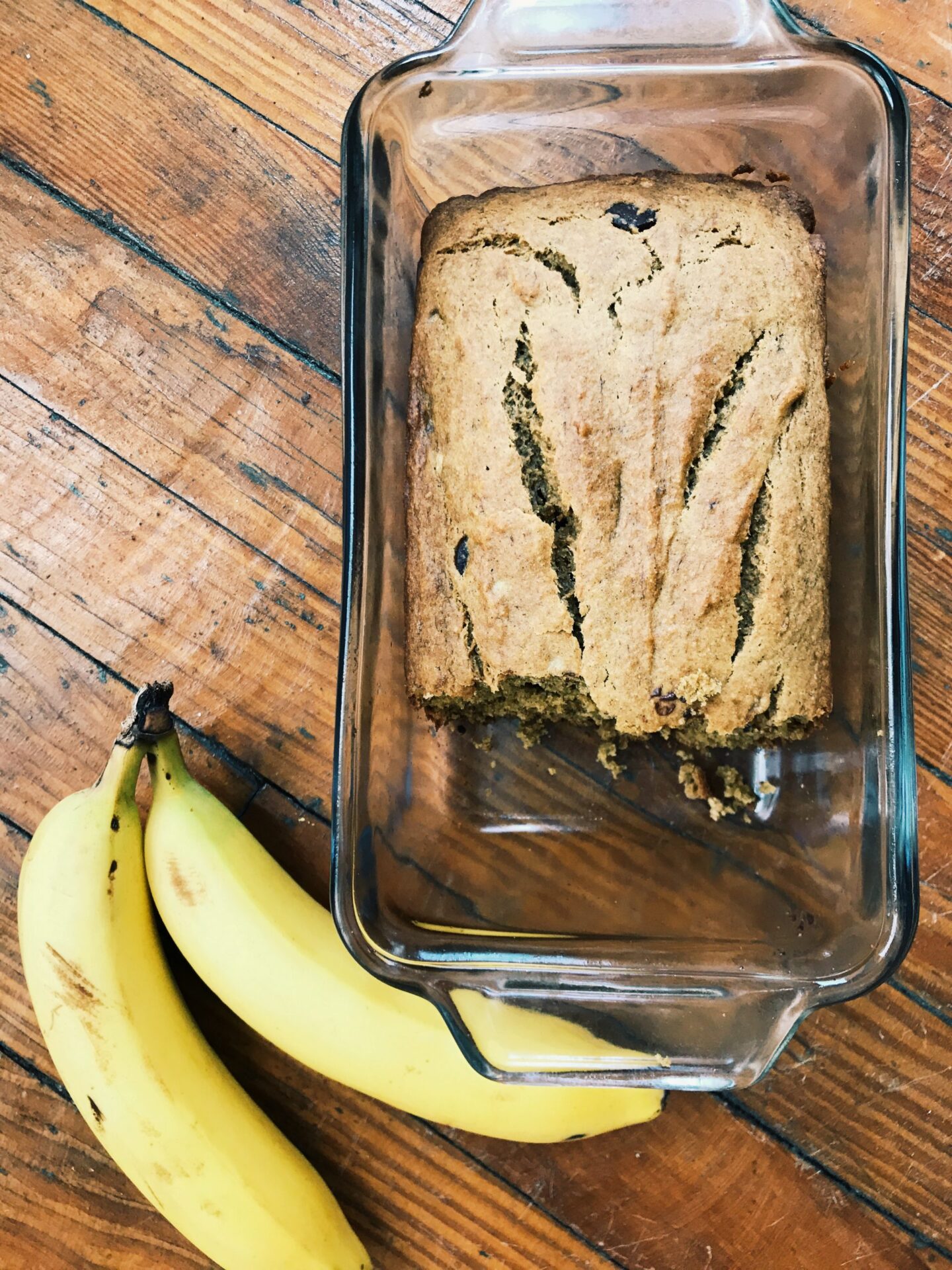 chocolate chip banana bread in loaf pan next to two bananas