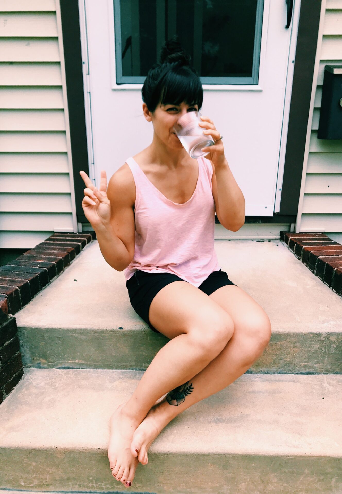 woman sitting on front steps in summer drinking a glass of water