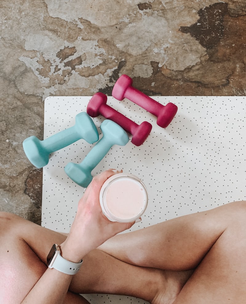 woman sitting on yoga mat with smoothie free weights and apple watch