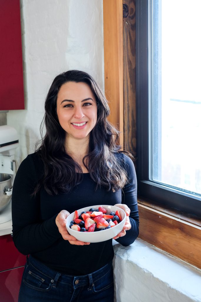 woman registered dietitian nutritionist posing with bowl of fresh strawberries and blueberries next to window