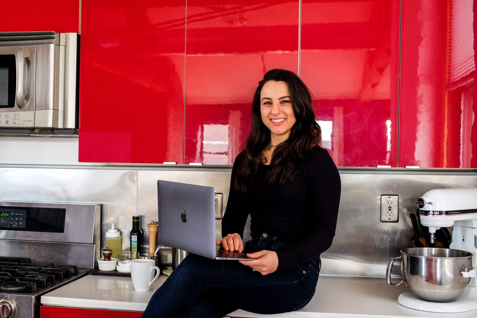 woman registered dietitian nutritionist sitting on counter smiling with laptop computer