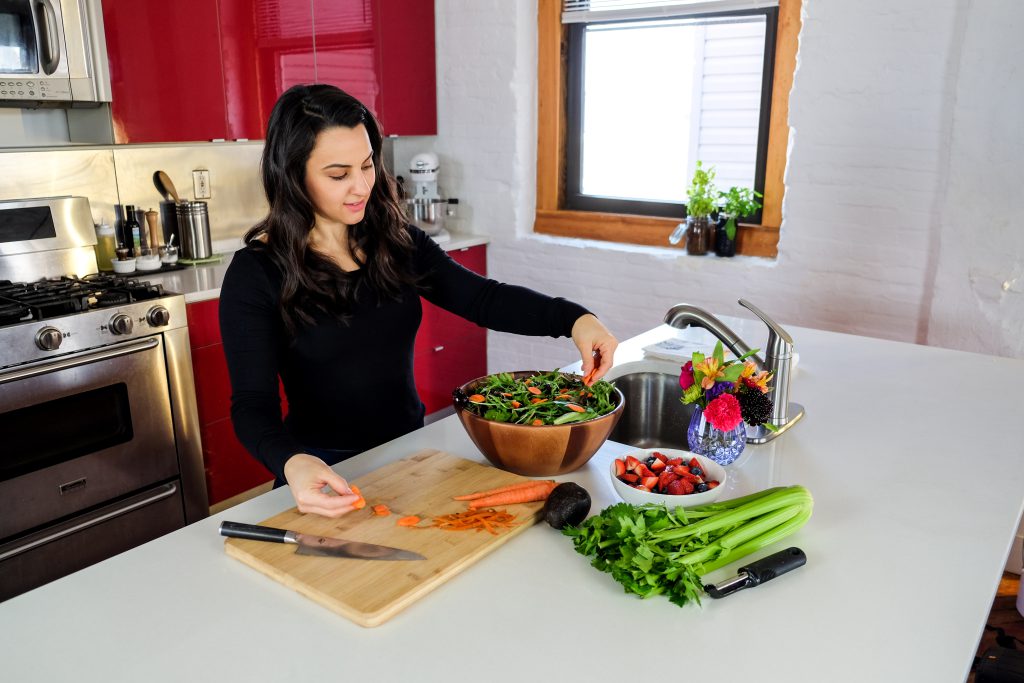 Woman arranging sliced carrots on a green salad in a wooden bowl